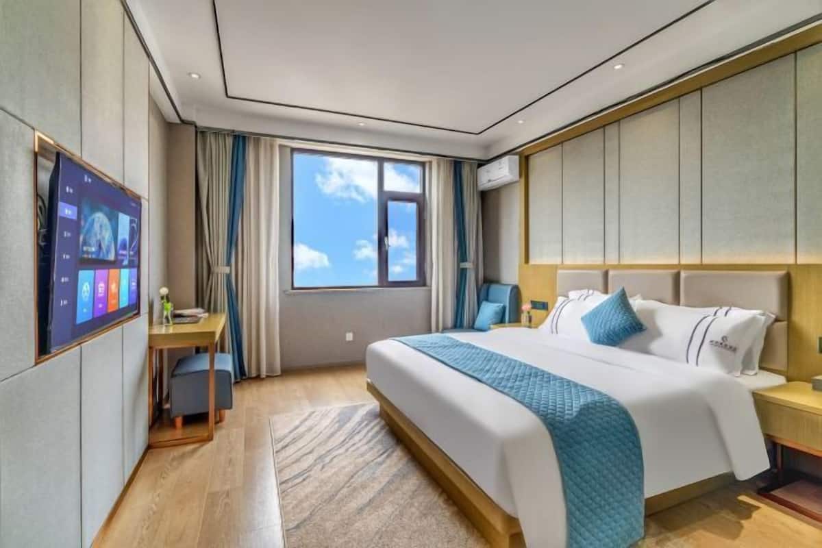 Een moderne hotelkamer met een groot bed, een bureau, een televisie en een raam met uitzicht op de lucht.