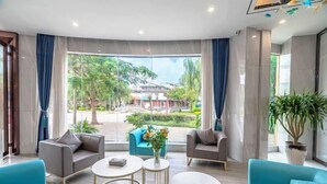 A modern hotel lobby with a large window offering a view of the outdoors, including a garden and buildings. There are several seating areas with sofas and tables. - Ningyu Lianchuang Business Hotel (Ning'er)