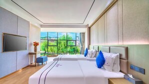 A modern hotel room with a large bed, a flat-screen TV, a bedside table, and a view of greenery outside. - Ningyu Lianchuang Business Hotel (Ning'er)
