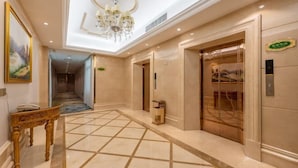 A hotel lobby with a chandelier, a reception desk, and an elevator. - Vienna International Hotel (Guangzhou Xintang High Speed Railway Station Cowboy City Branch) (Guangzhou)