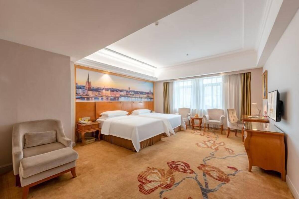 A hotel room with a large bed, a sofa, a desk, and a television.