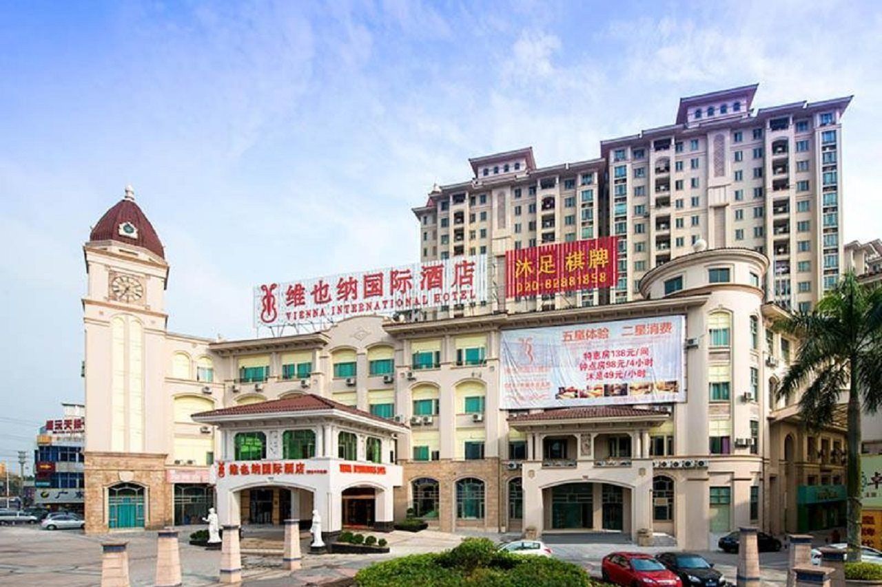 A multi-story hotel with a prominent clock tower, a large signboard, and a well-maintained entrance area.