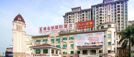 A multi-story hotel with a prominent clock tower, a large signboard, and a well-maintained entrance area.