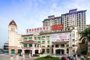 A multi-story hotel with a prominent clock tower, a large signboard, and a well-maintained entrance area. - Vienna International Hotel (Guangzhou)