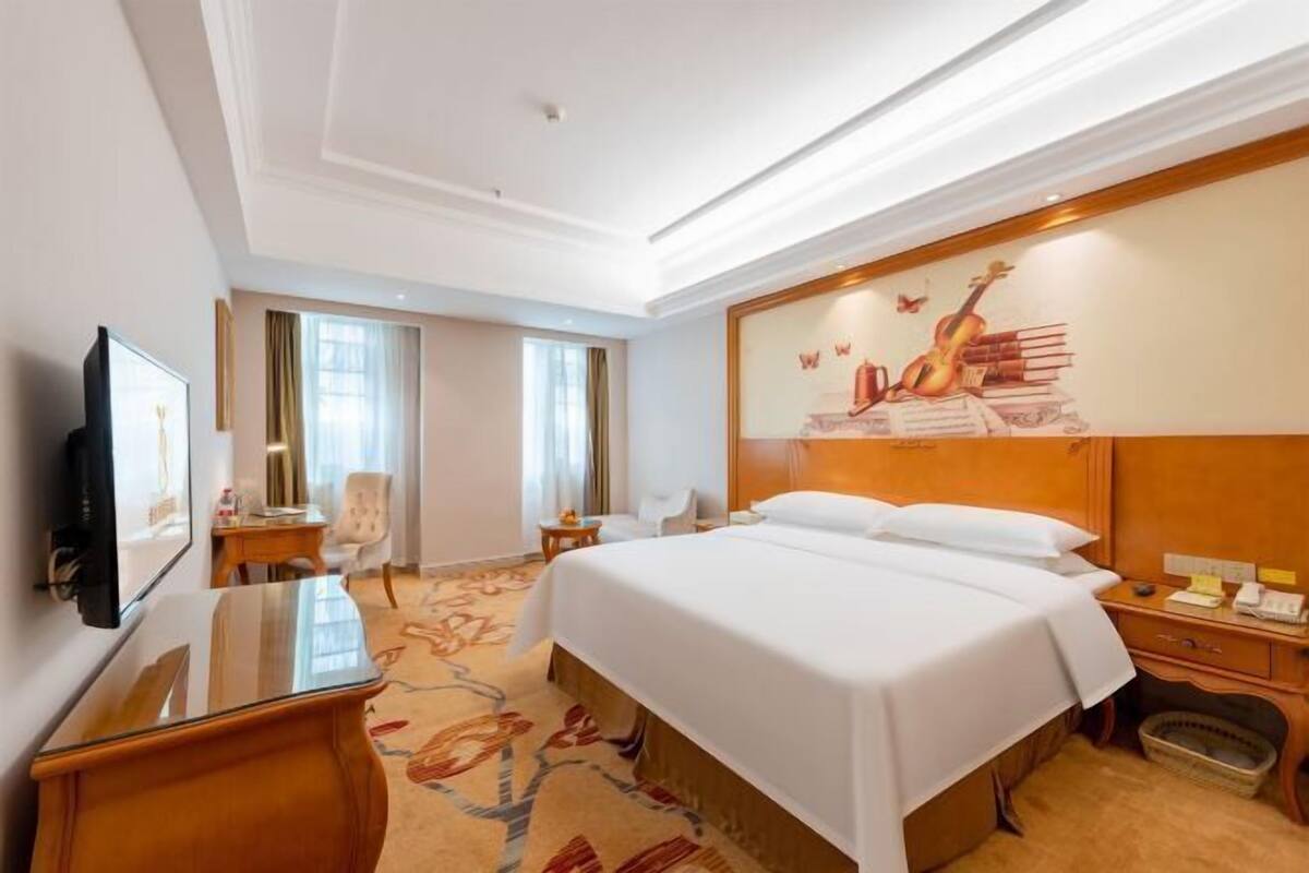 A hotel room with a large bed, a desk, a chair, a television, and a painting on the wall.
