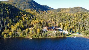A lodge with a large roof and multiple windows, surrounded by dense forest and a lake. - Auberge Boréale de Charlevoix (Petit-Saguenay)