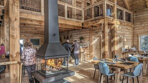 Een rustiek houten interieur met een centraal gelegen open haard, een eiken houten eetgedeelte en hoge plafonds.