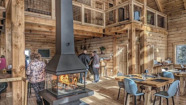 A rustic wooden interior with a central fireplace, wooden dining area, and high ceilings. - Auberge Boréale de Charlevoix (Petit-Saguenay)