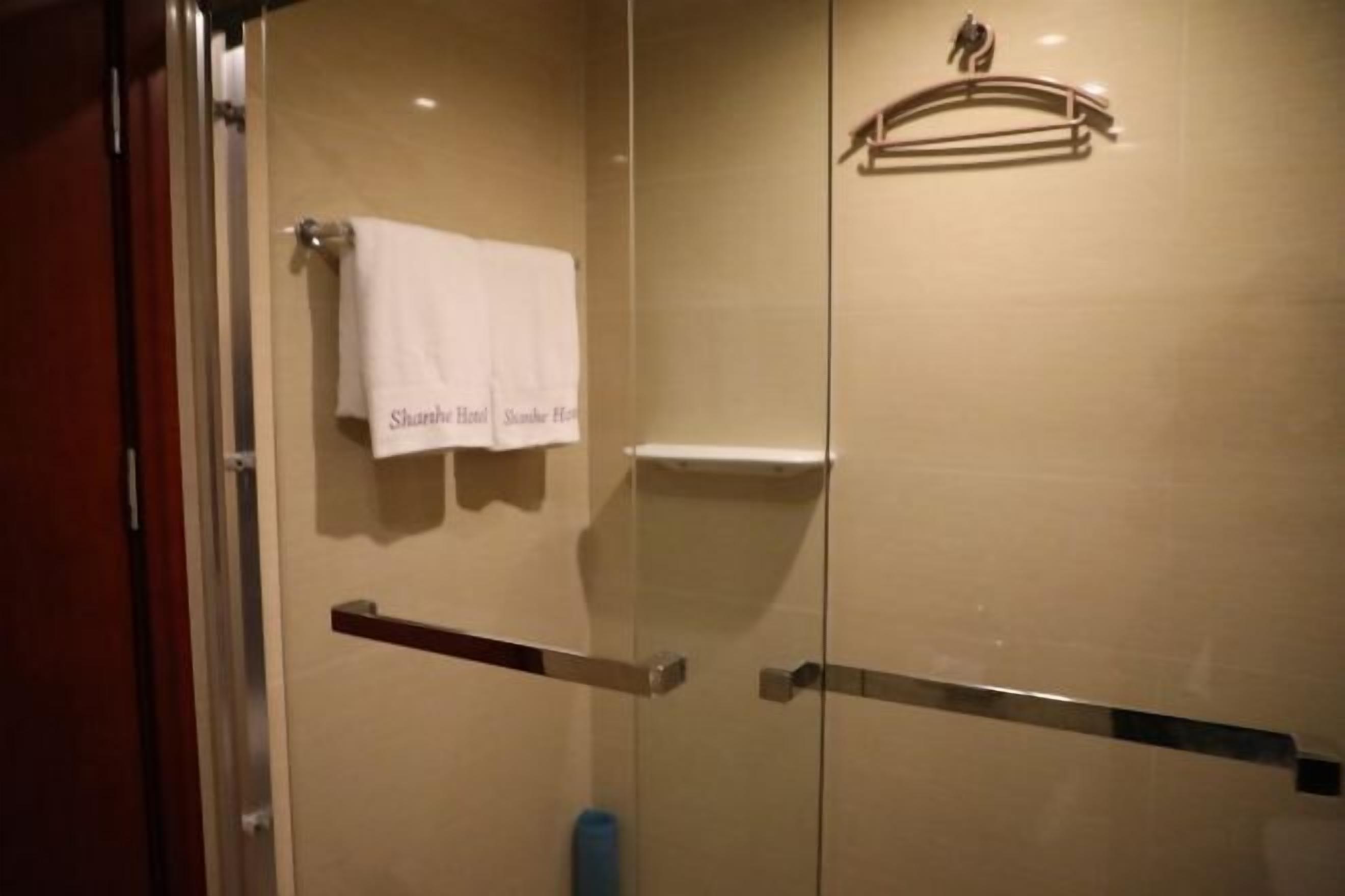Une salle de bain d’hôtel avec une douche à parois de verre, un porte-serviettes avec une serviette blanche et un pommeau de douche.