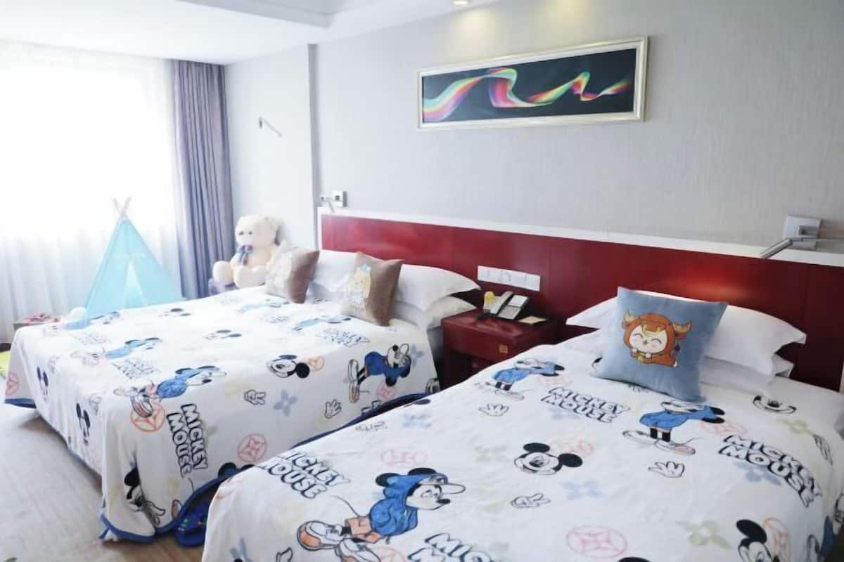 A hotel room with two beds, each with Mickey Mouse-themed bedding. There is a blue teepee, a teddy bear, and a painting on the wall.