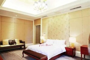 Une chambre d’hôtel avec un grand lit, une banquette, deux tables de chevet et un lustre.