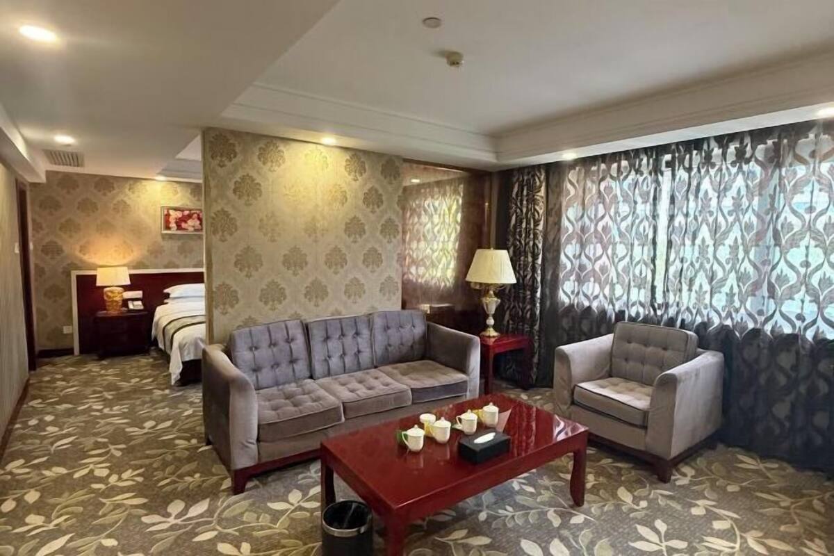 A hotel room with a sofa, armchair, and a table with teapots.