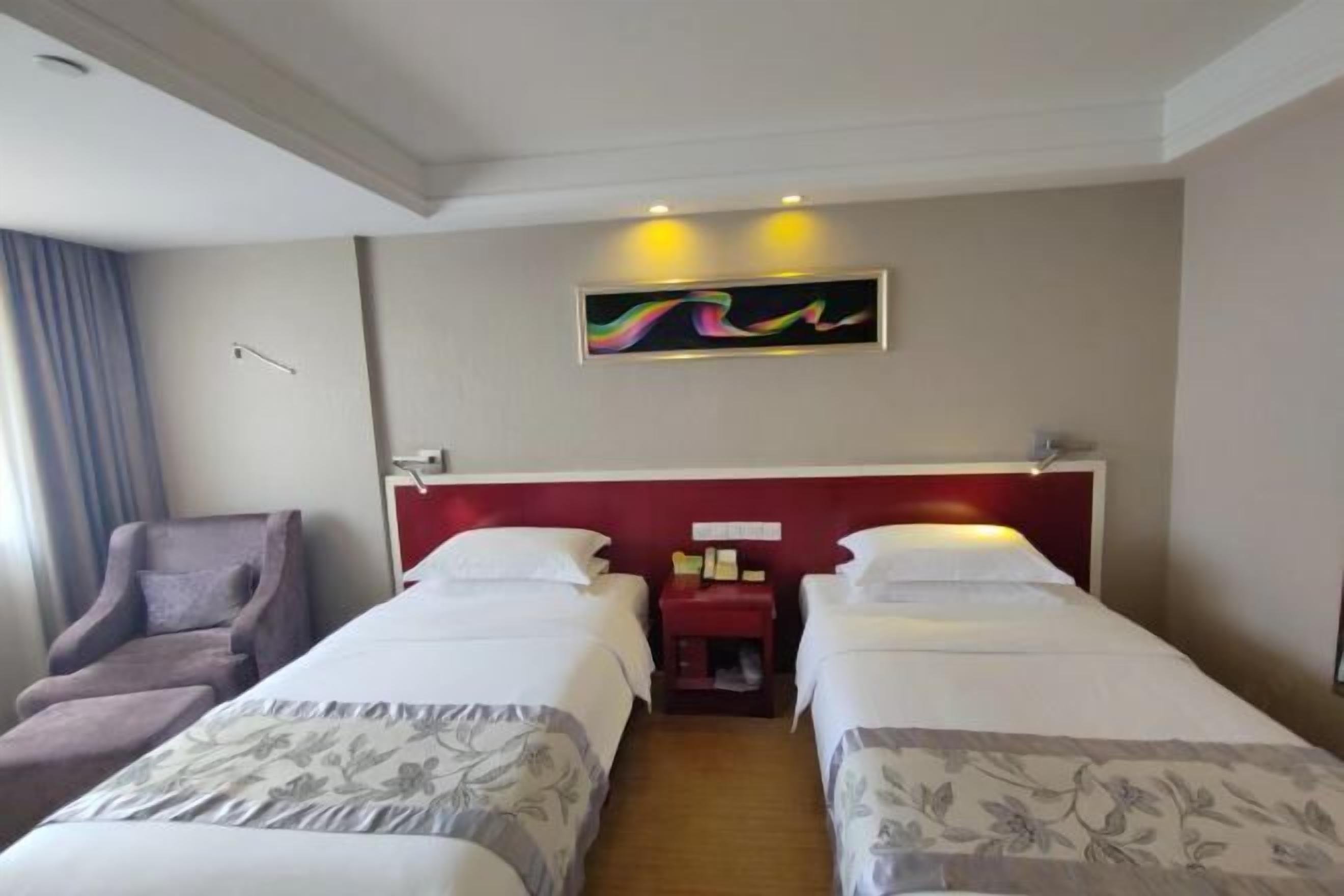 Une chambre d’hôtel avec deux lits, une tête de lit rouge, une petite table avec une lampe et une chaise.