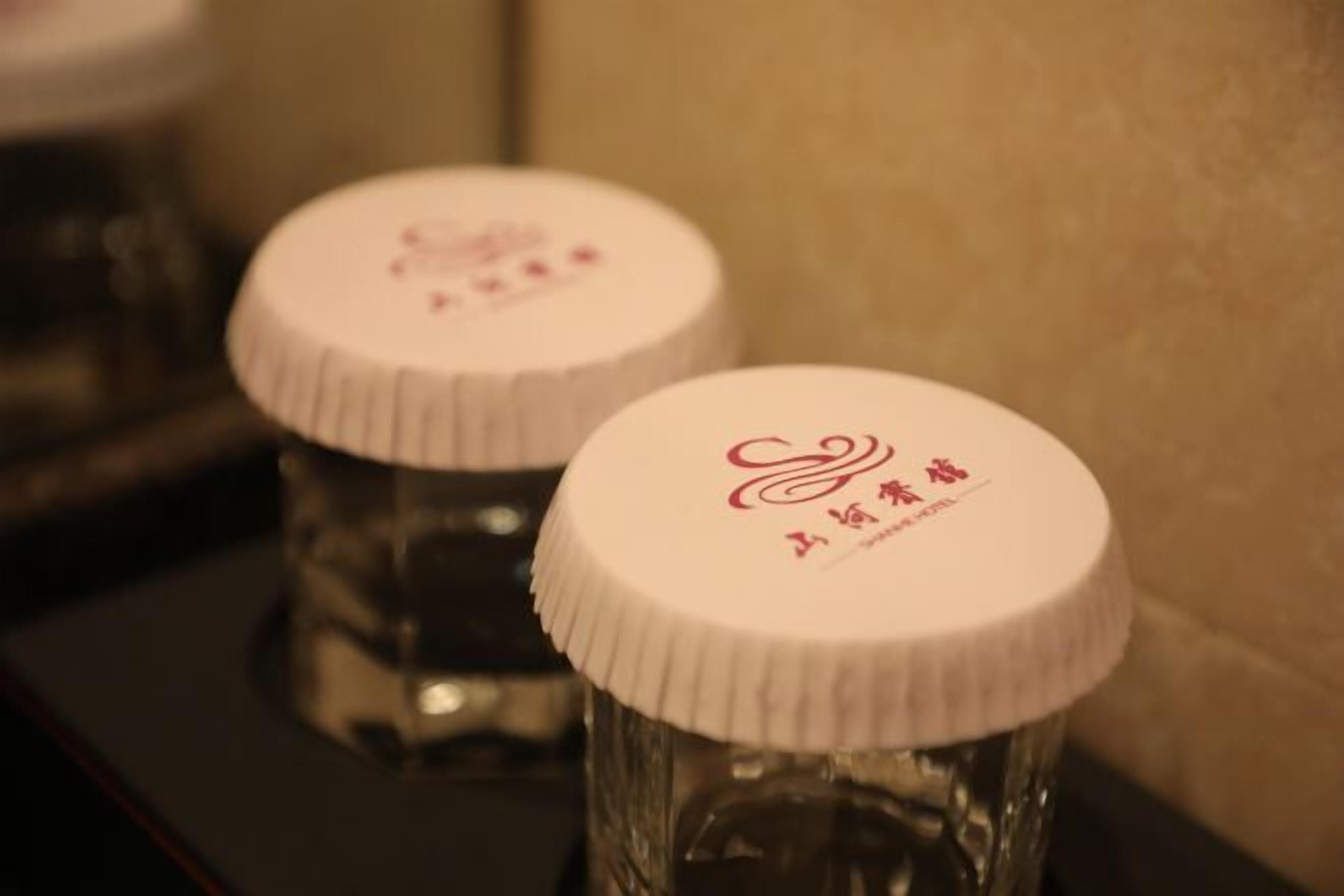 Dos botellas de vidrio transparente con tapas blancas, cada una con un logotipo y texto en rojo.