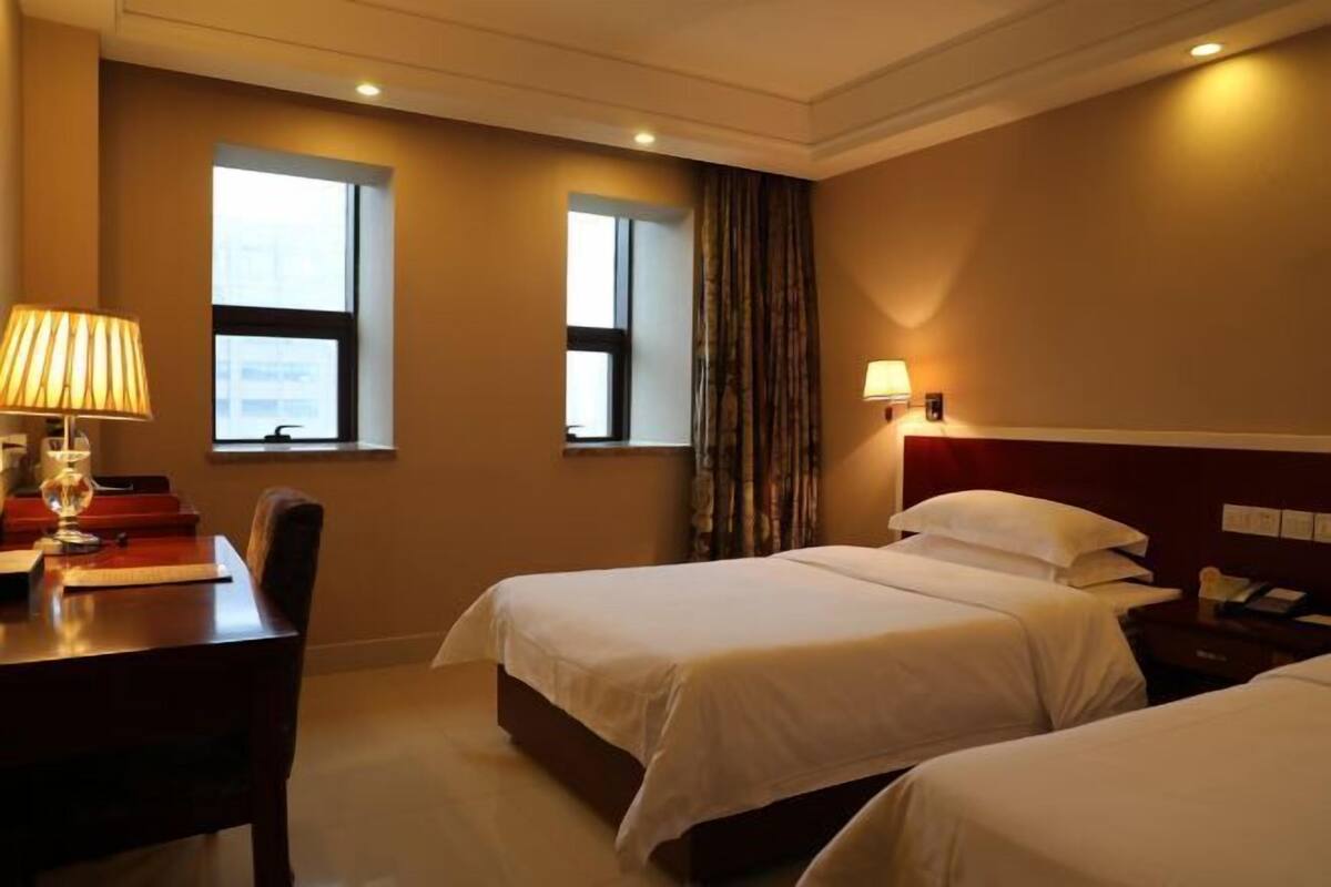 A hotel room with two beds, a desk, and a chair. There are windows and a curtain.