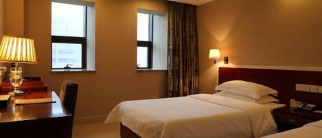 A hotel room with two beds, a desk, and a chair. There are windows and a curtain.