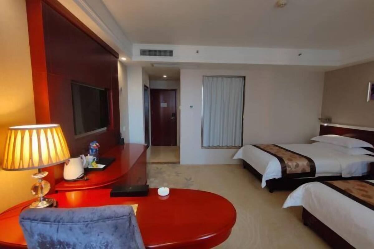 A hotel room with a TV, two beds, a red table, and a lamp.