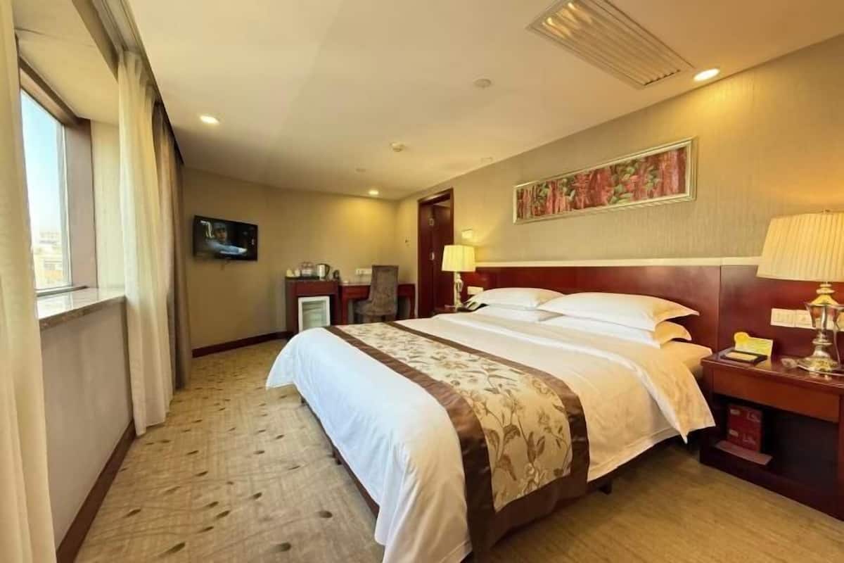 A hotel room with a large bed, a television, a desk with a lamp, and a painting on the wall.