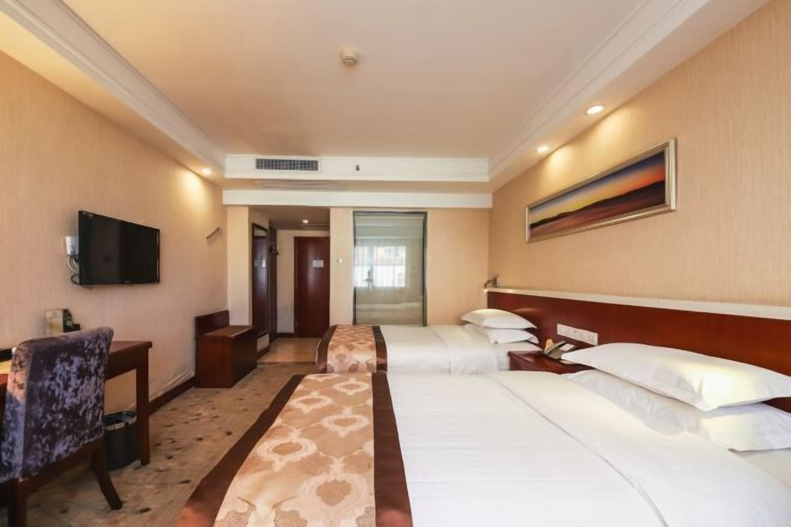 Habitación de hotel con dos camas, televisión, escritorio y un cuadro en la pared.