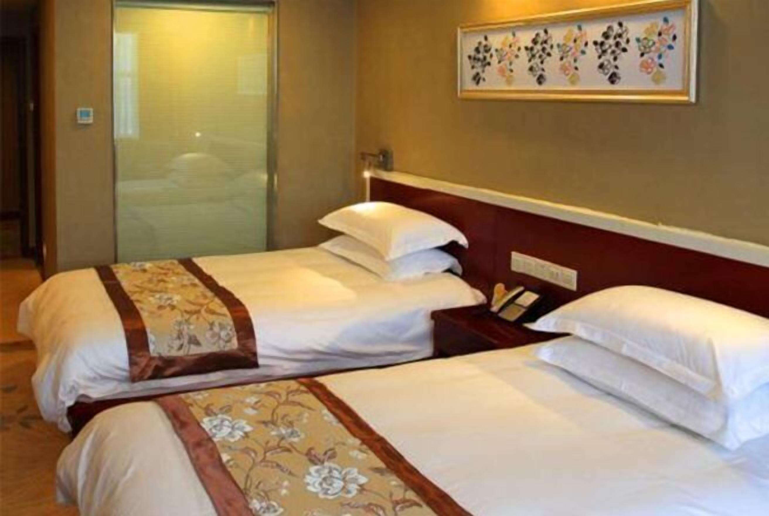 A hotel room with two beds, each with a floral bedspread and a wooden headboard.