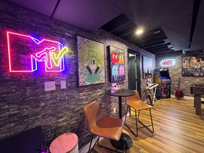 Een kamer met een neonreclame, een muur met een muurschildering, een jukebox en een gitaar.