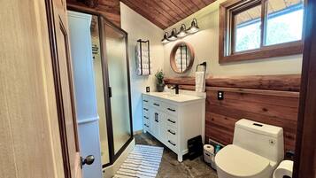 Une salle de bain avec un lavabo blanc, un meuble-lavabo en bois, des toilettes et un espace douche.