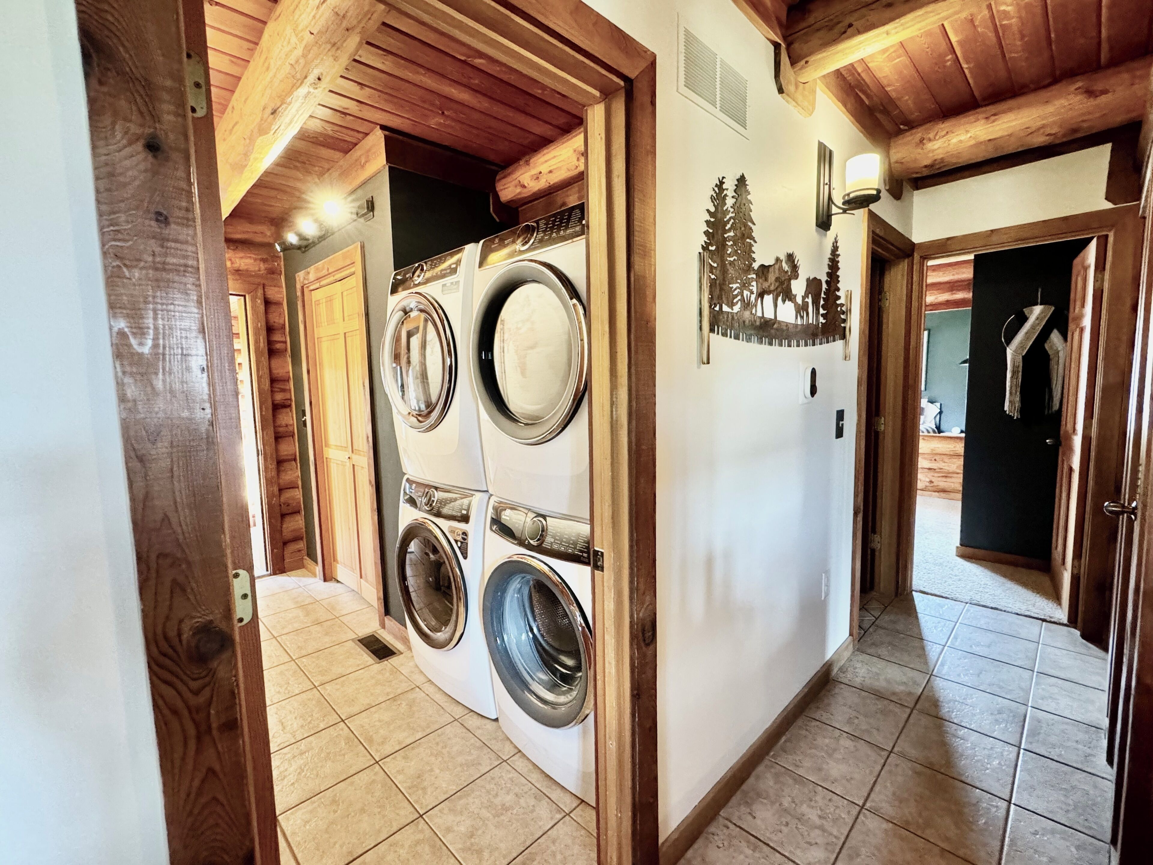 Une buanderie avec des lave-linge et des sèche-linge superposés, des poutres en bois et un décor mural représentant un arbre.