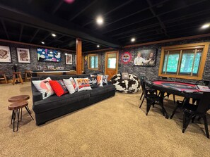 A room with a black leather sofa, a pool table, and a bar area.