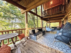 A wooden deck with outdoor seating, including a table and chairs, and a hanging chair.