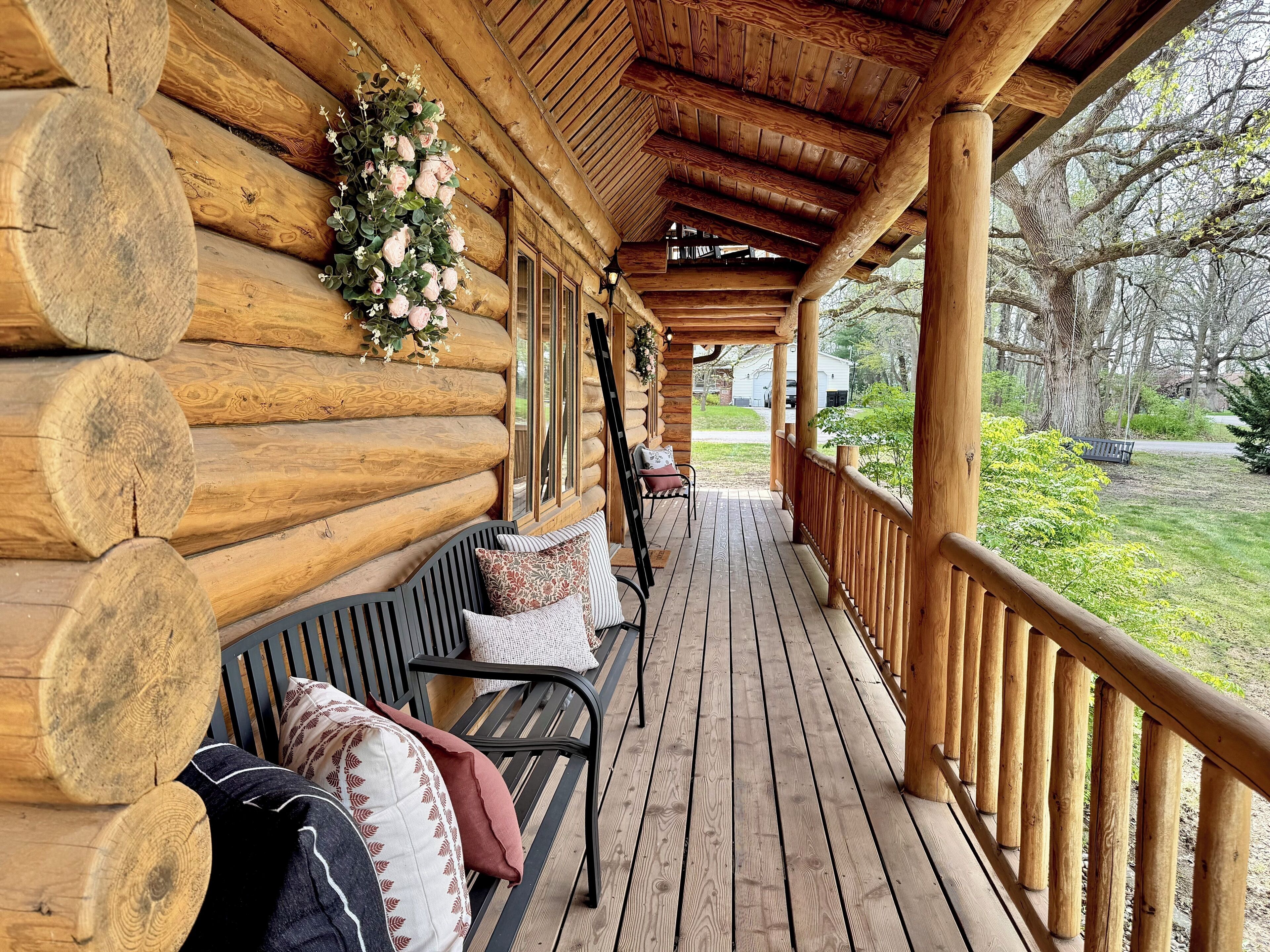Une cabane en rondins avec une véranda en bois, un banc et un arrangement floral.