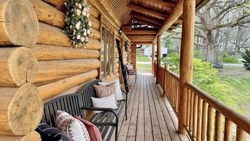 A log cabin with a wooden porch, a bench, and a flower arrangement.