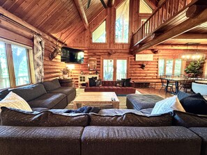 A log cabin interior with a living room, dining area, and a TV mounted on the wall.
