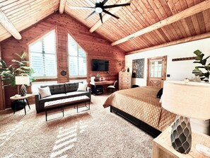 Een gezellige kamer met een houten plafond, een bed, een bureau en een televisie.
