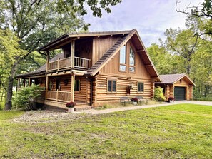A log cabin with a balcony, a garage, and a small attached building.