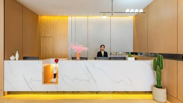 A reception desk with a receptionist, a potted plant, and a wall-mounted light fixture. - Floral Hotel·Yangshuo Shiyin Yue Hotel (Yangshuo Xijie Shili Hualang Branch) (Yangshuo)