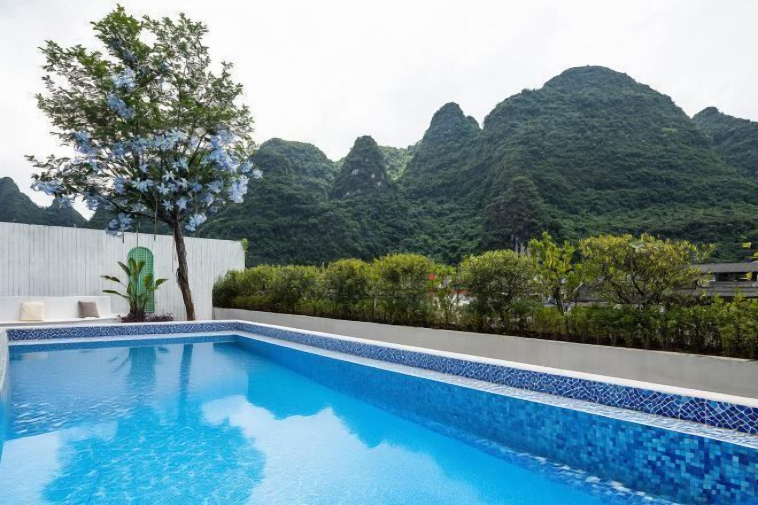 A swimming pool with a tiled edge, surrounded by greenery and a mountainous backdrop.