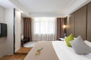 A hotel room with a bed, a TV, a desk with a chair, a window with curtains, and a nightstand with a lamp. - Floral Hotel·Yangshuo Shiyin Yue Hotel (Yangshuo Xijie Shili Hualang Branch) (Yangshuo)