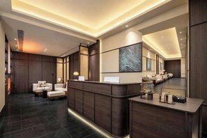 A modern reception area with a wooden reception desk, seating area, and a large abstract painting on the wall.