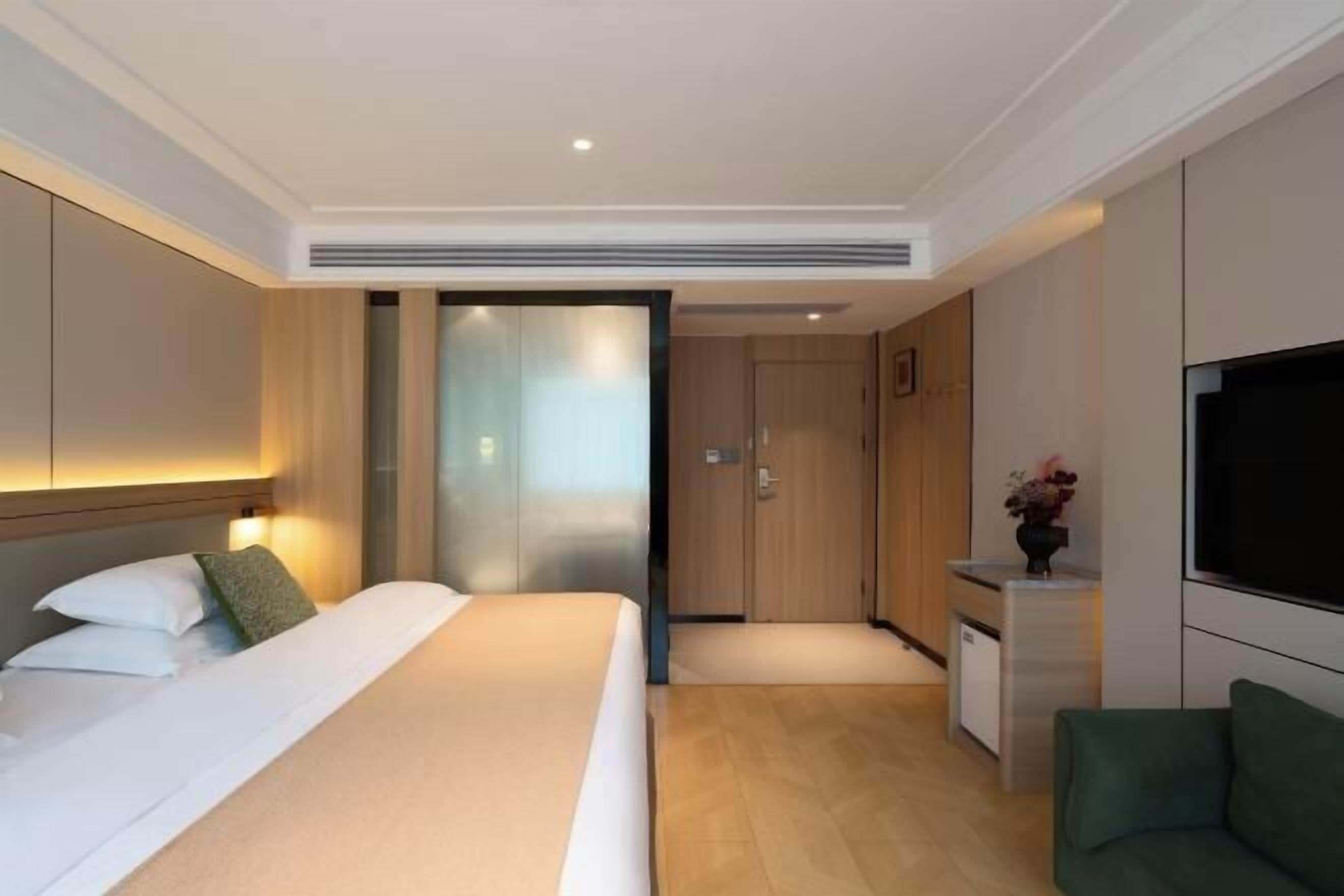 A hotel room with a bed, bedside table, TV, and a small kitchenette.