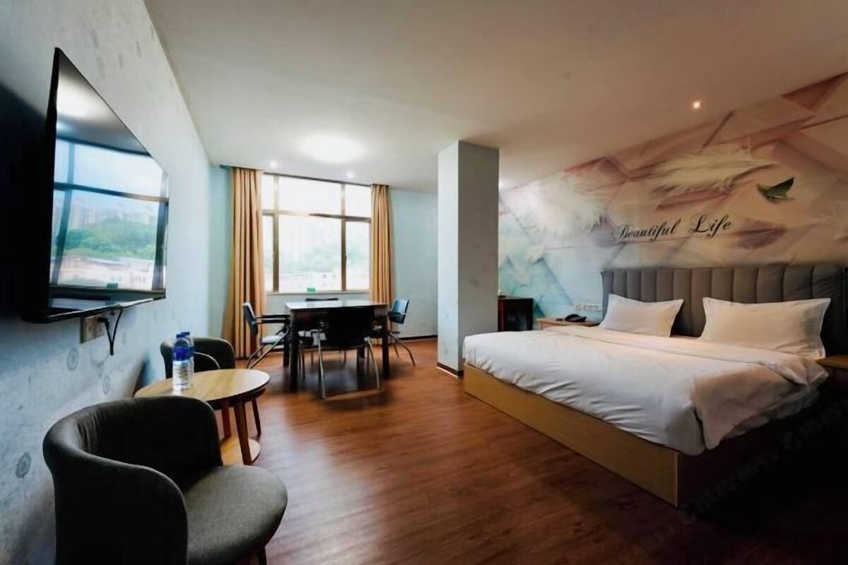 A hotel room with a bed, a desk, a chair, a TV, and a mural on the wall.