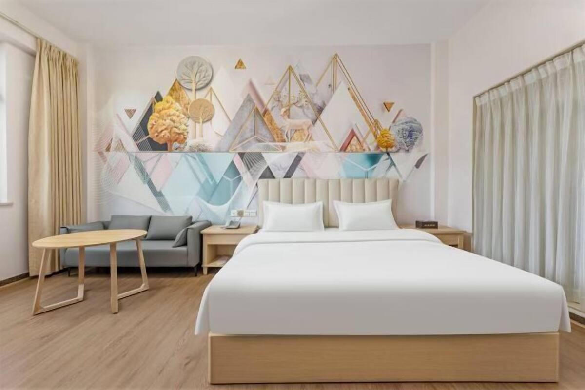 A hotel room with a bed, a desk, a sofa, and a wall with geometric artwork.