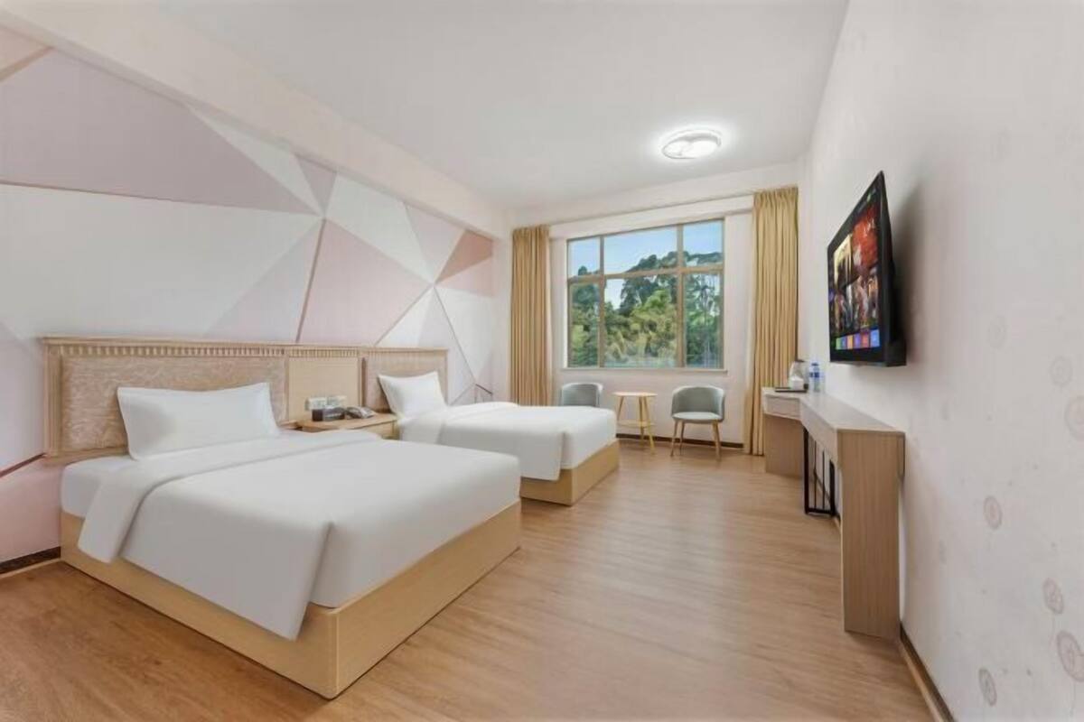 A hotel room with two beds, a desk, a chair, a TV, and a window with a view.