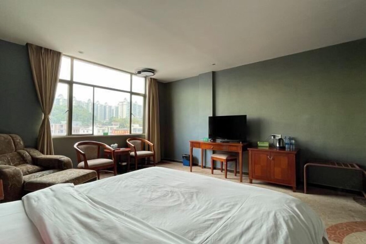 Een hotelkamer met een groot bed, een bureau met een televisie, twee stoelen en uitzicht op de stad door het raam.