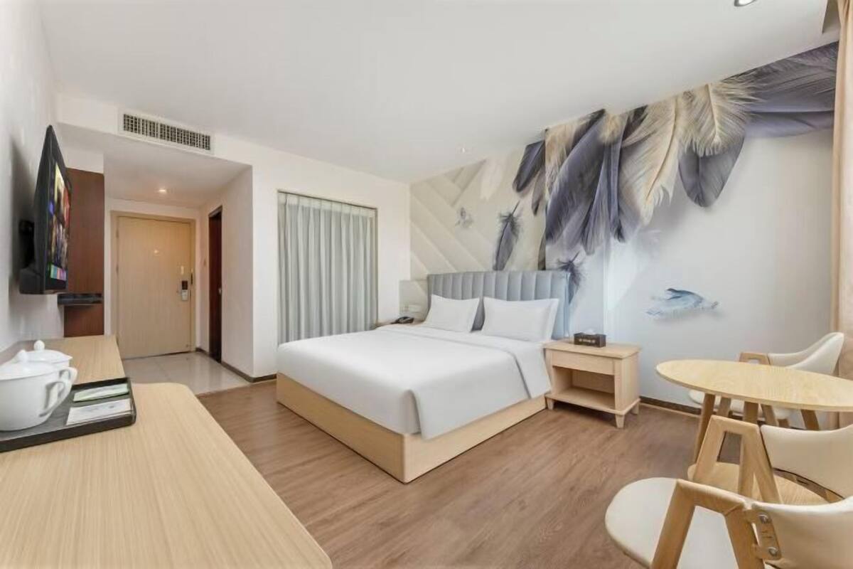 A hotel room with a bed, bedside table, chair, and a wall with feather artwork.