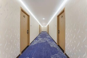 Un couloir d'hôtel avec des revêtements de sol en moquette, des portes en bois et des motifs décoratifs sur les murs.
