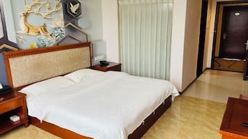 A hotel room with a large bed, a bedside table, a nightstand, a decorative wall piece, and a window with curtains.
