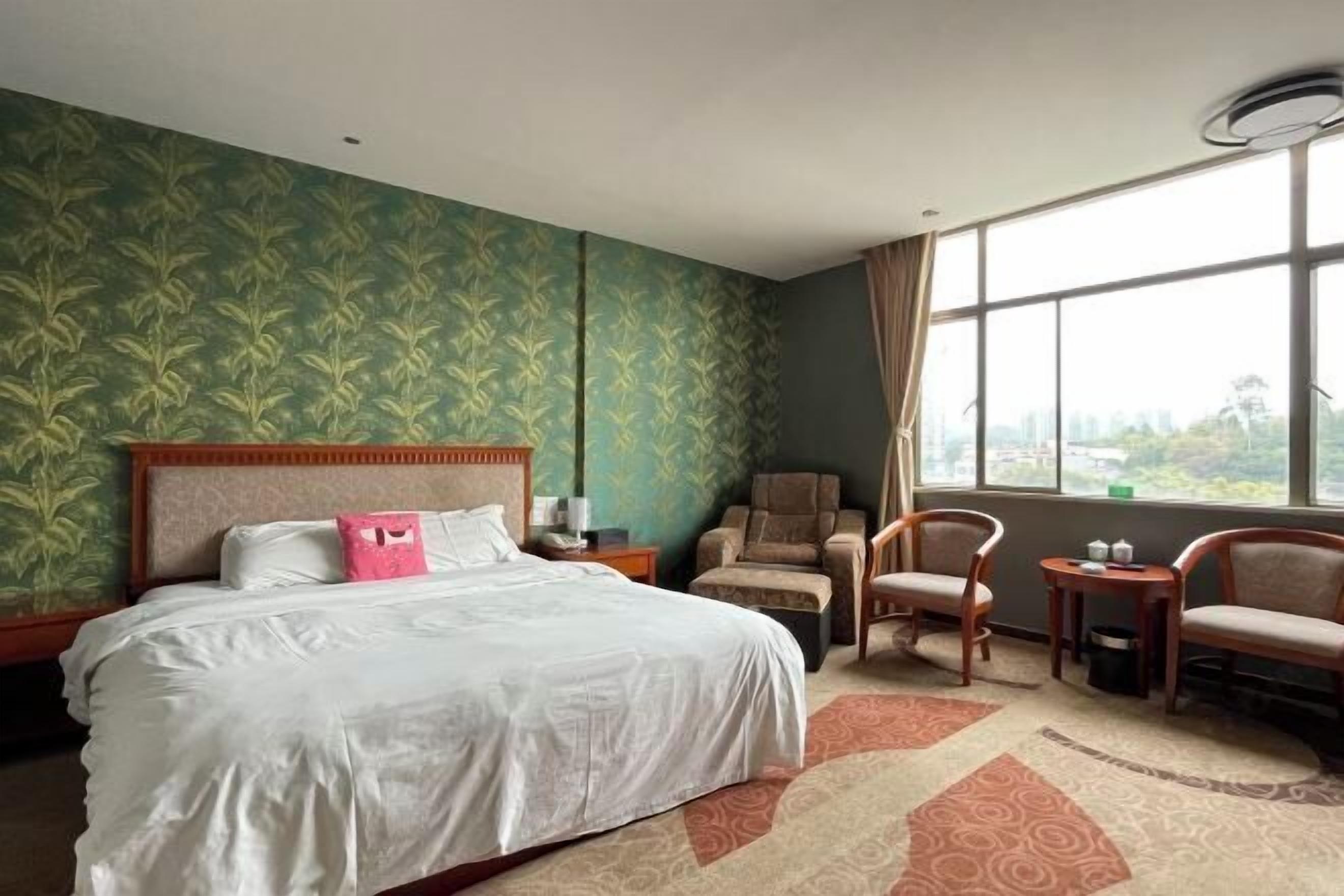 A hotel room with a large bed, two armchairs, a small table, and a window with a city view.