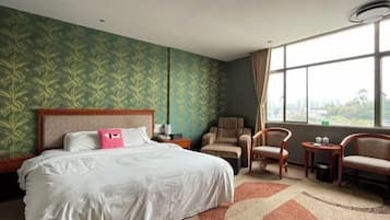 A hotel room with a large bed, two armchairs, a small table, and a window with a city view.