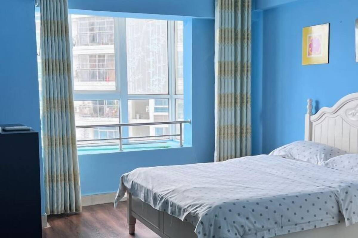 A bedroom with a bed, a window with curtains, and a blue wall.