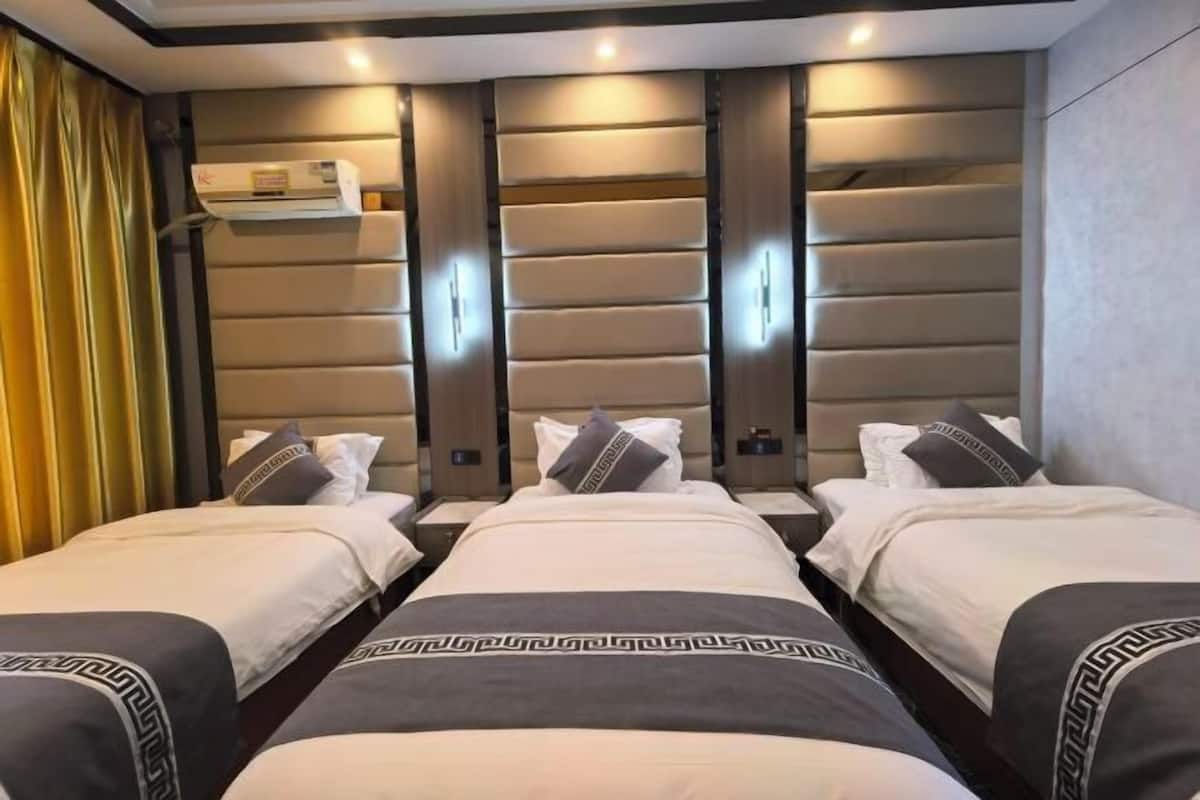 Quarto de hotel com três camas, um minibar e uma prateleira fixada na parede.